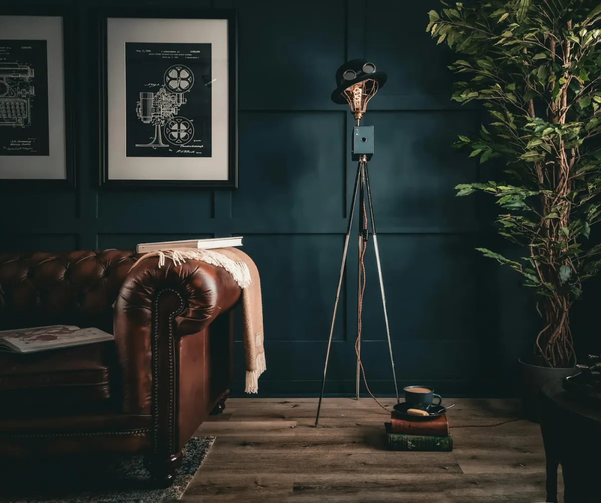 A leather sofa and a tripod floor lamp against a dark panelled wall A leather sofa and a tripod floor lamp against a dark panelled wall