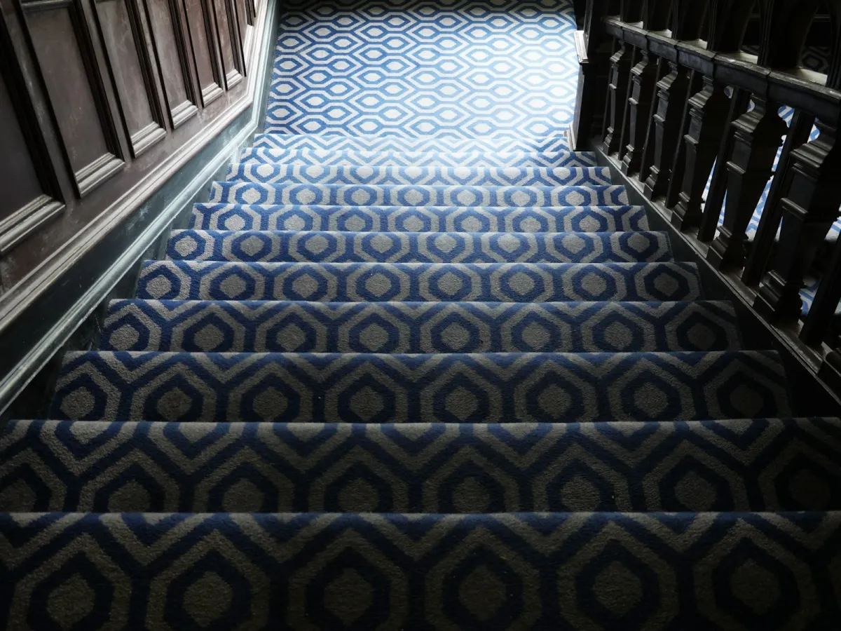A staircase covered in blue and grey patterned carpet with dark wooden banisters A staircase covered in blue and grey patterned carpet with dark wooden banisters