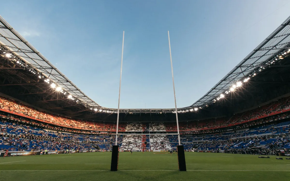 Rugby goal posts on a green pitch inside a large stadium with crowded stands Rugby goal posts on a green pitch inside a large stadium with crowded stands
