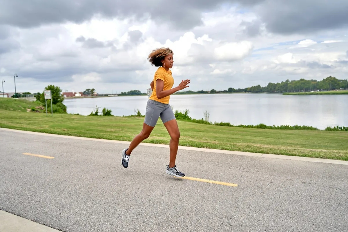 A woman in a yellow tee and grey shorts running along a lakeside path A woman in a yellow tee and grey shorts running along a lakeside path