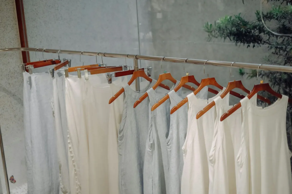 White and grey linen dresses and trousers hanging on wooden hangers along a rail White and grey linen dresses and trousers hanging on wooden hangers along a rail