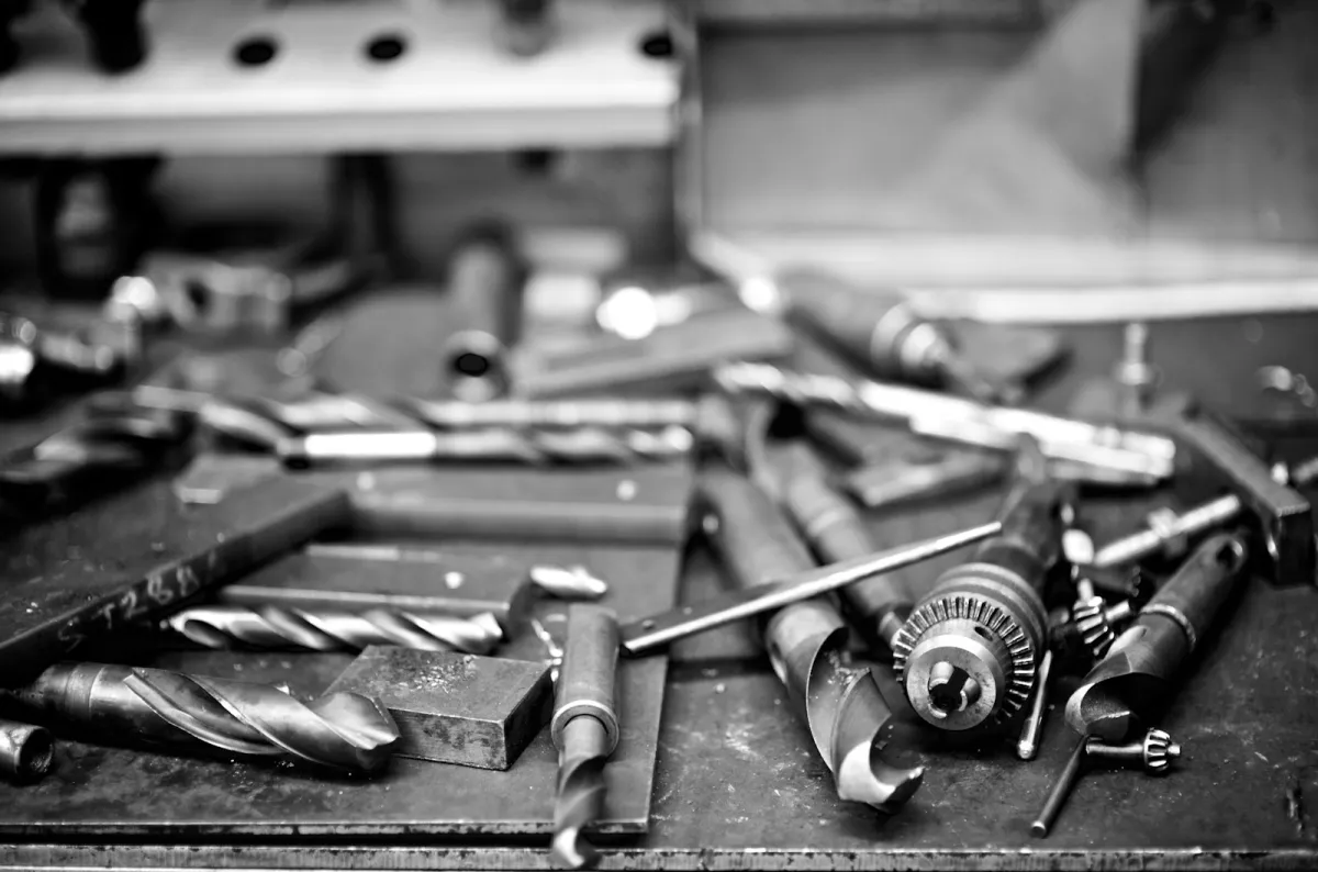 Black and white close-up of drill bits and a drill chuck on a workshop bench Black and white close-up of drill bits and a drill chuck on a workshop bench