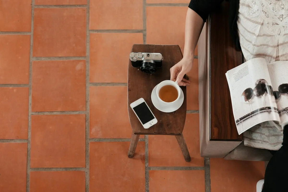 Overhead view of a cup of tea on a wooden stool beside an open magazine on a bench