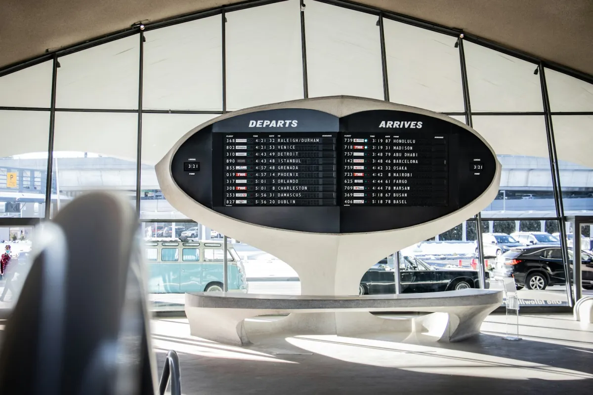Departures and arrivals board in an airport terminal with cars parked outside Departures and arrivals board in an airport terminal with cars parked outside