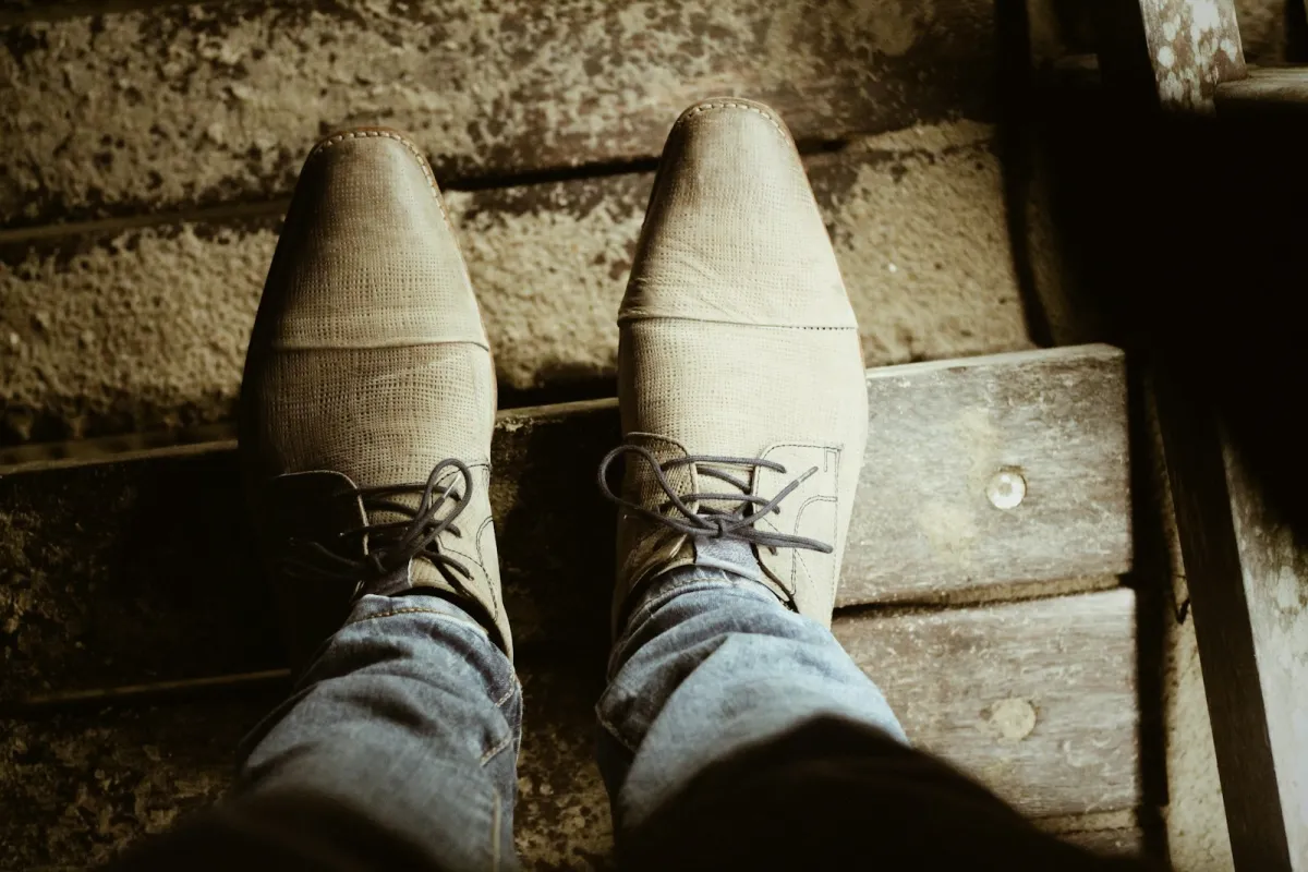 Looking down at a pair of men's leather lace-up shoes and jeans on wooden steps