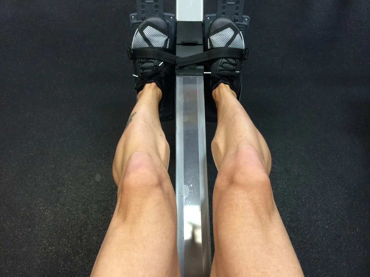 Looking down at legs and trainers strapped into the footrests of a rowing machine