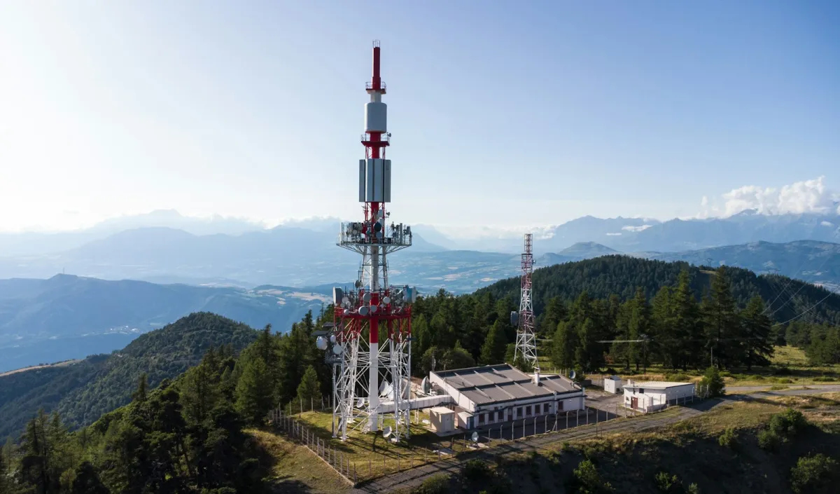 Radio mast on a forested hilltop with mountains behind