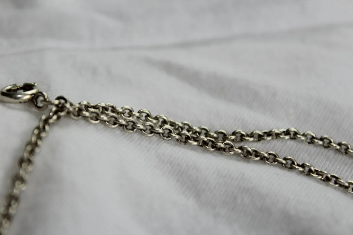 Silver chain necklace with a clasp lying on white fabric