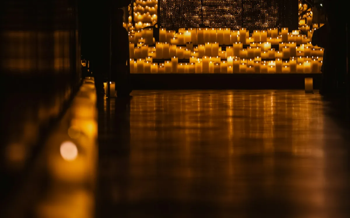 Rows of lit candles glowing in a dark room Rows of lit candles glowing in a dark room