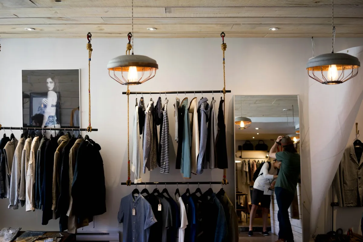Rails of coats and shirts hanging in a bright clothing boutique with pendant lamps