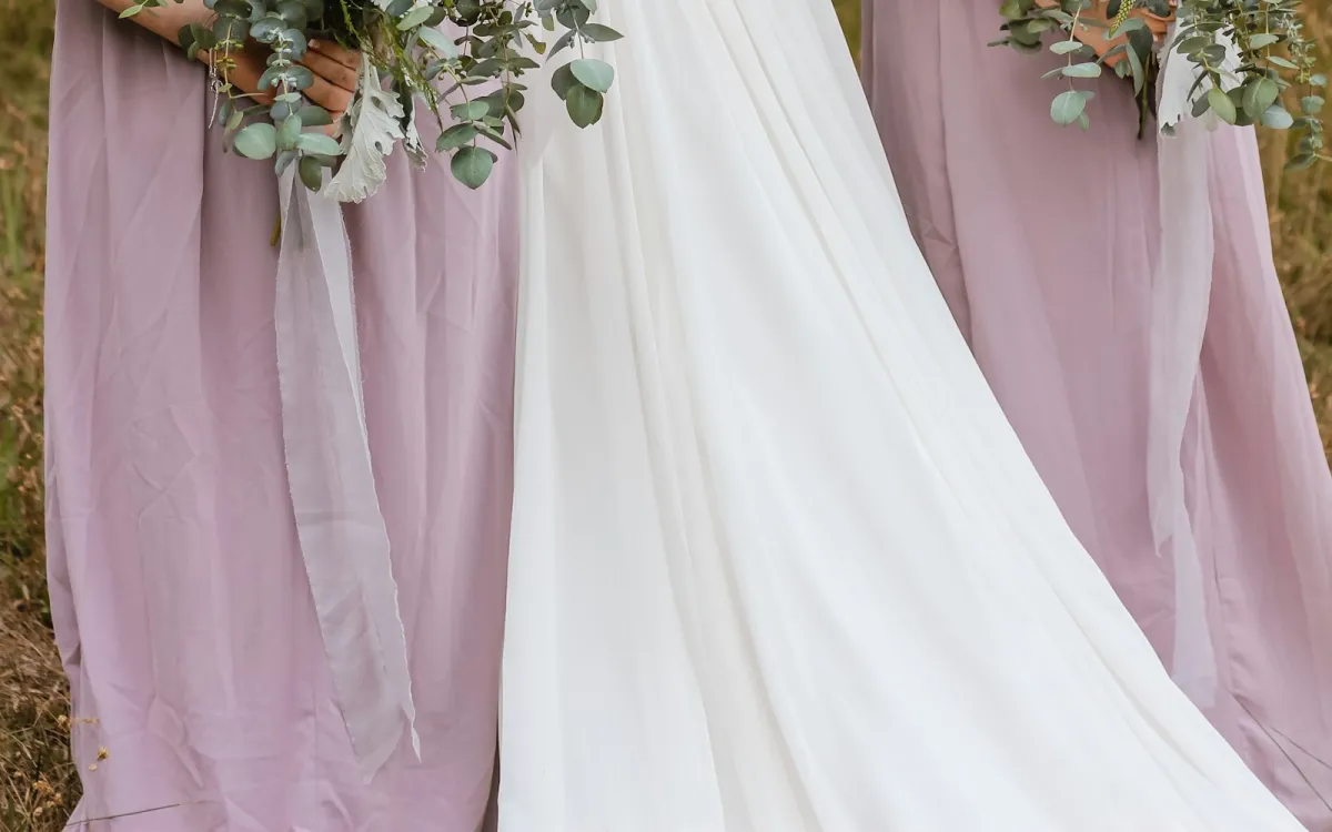 Bridesmaids in long lilac chiffon dresses holding eucalyptus bouquets beside a bride's flowing white gown Bridesmaids in long lilac chiffon dresses holding eucalyptus bouquets beside a bride's flowing white gown