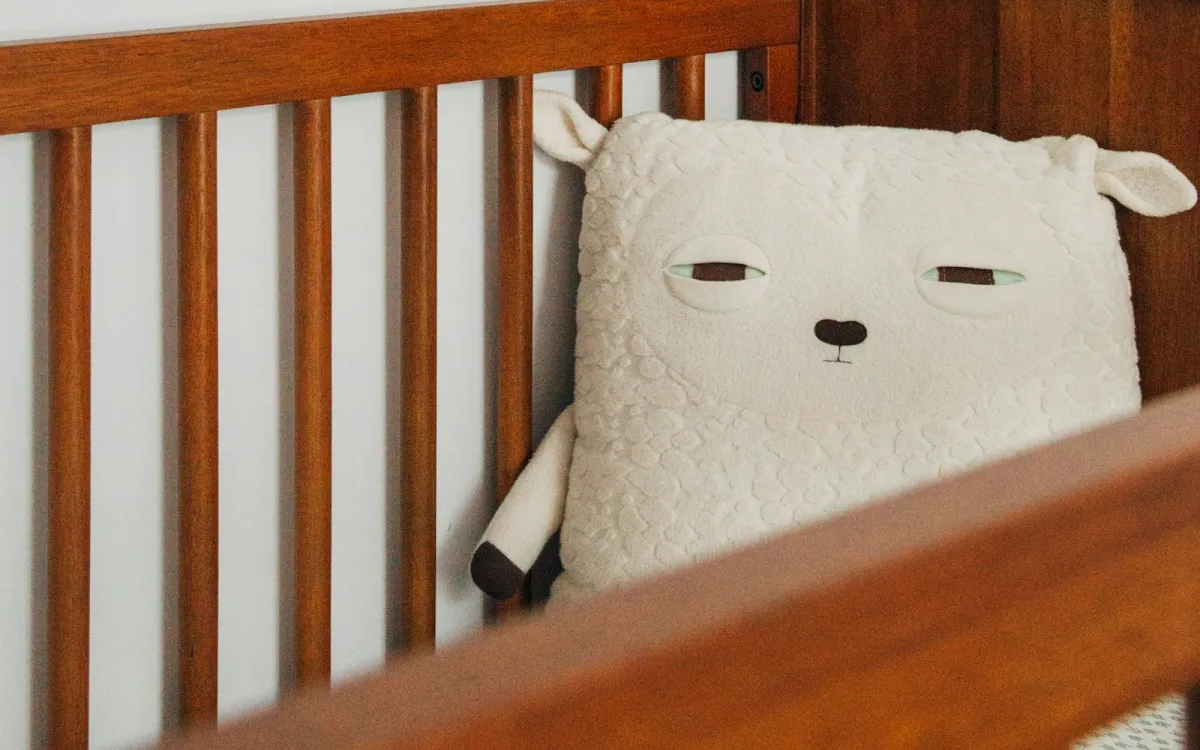 Wooden cot with a soft sheep cushion in a white nursery Wooden cot with a soft sheep cushion in a white nursery
