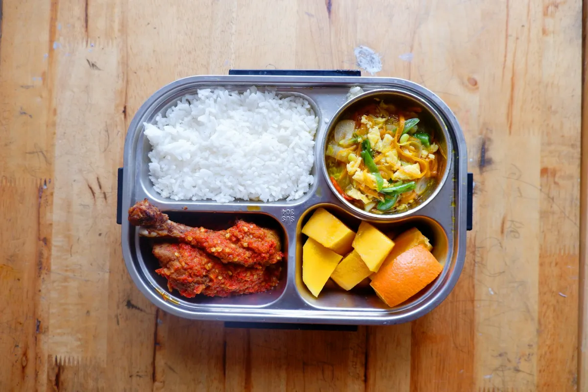 A partitioned lunch box filled with rice, chicken, curry and fruit