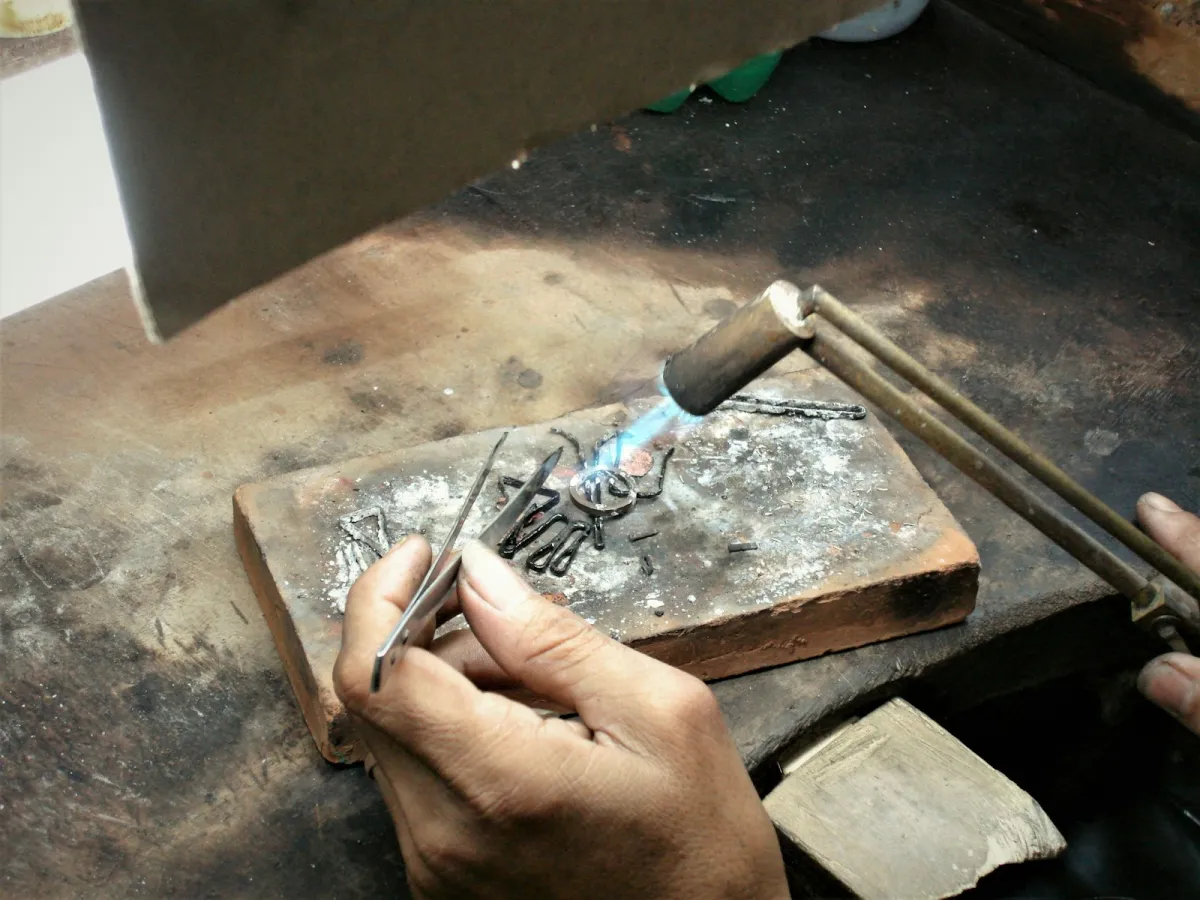 A jeweller's hands holding tweezers while soldering a ring with a small blue flame on a workbench A jeweller's hands holding tweezers while soldering a ring with a small blue flame on a workbench