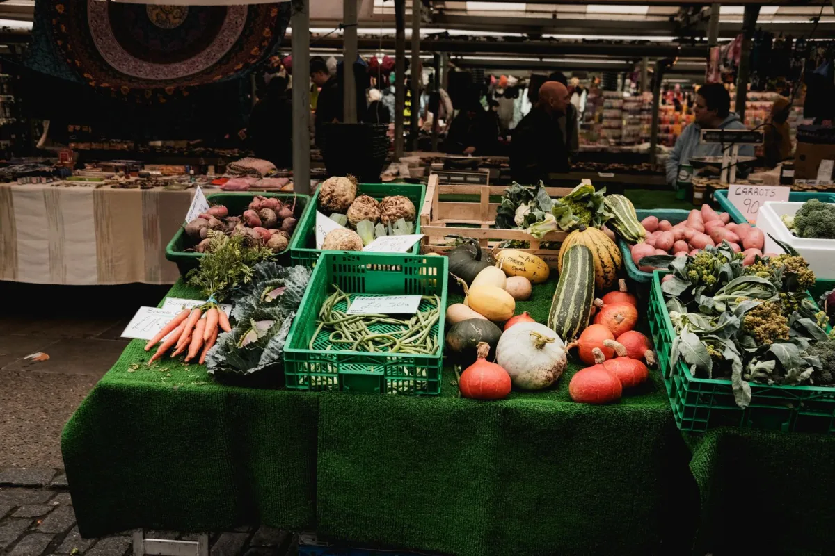 A market stall with crates of carrots, beetroot, green beans, squash and pumpkins on green matting A market stall with crates of carrots, beetroot, green beans, squash and pumpkins on green matting