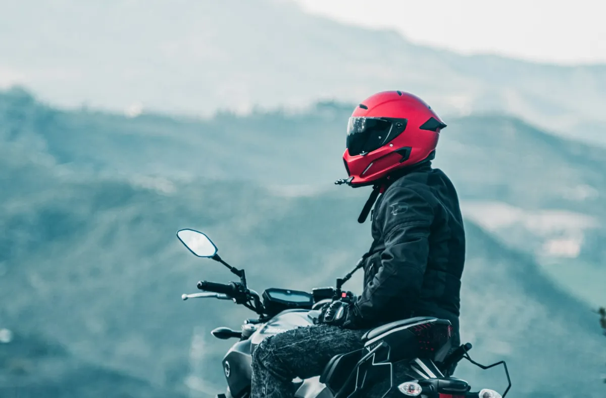A rider in a red helmet sitting on a motorbike with misty hills behind