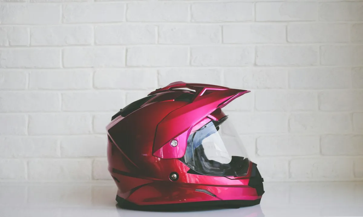 A glossy red adventure-style motorcycle helmet against a white brick wall A glossy red adventure-style motorcycle helmet against a white brick wall