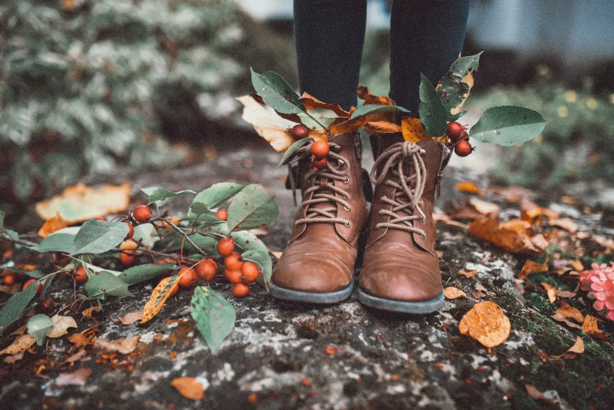 Brown lace-up boots on a mossy path scattered with autumn leaves and berries
