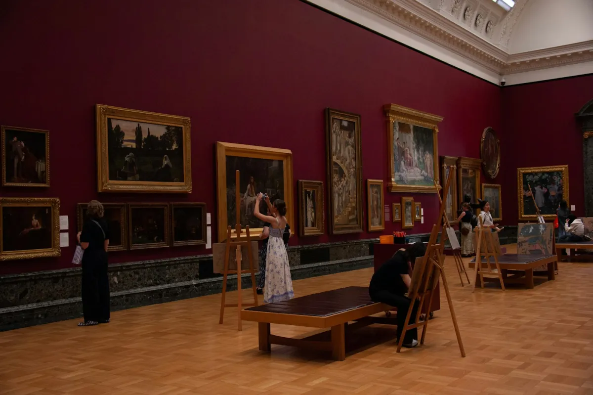 Visitors looking at paintings in gilt frames on a deep red gallery wall Visitors looking at paintings in gilt frames on a deep red gallery wall