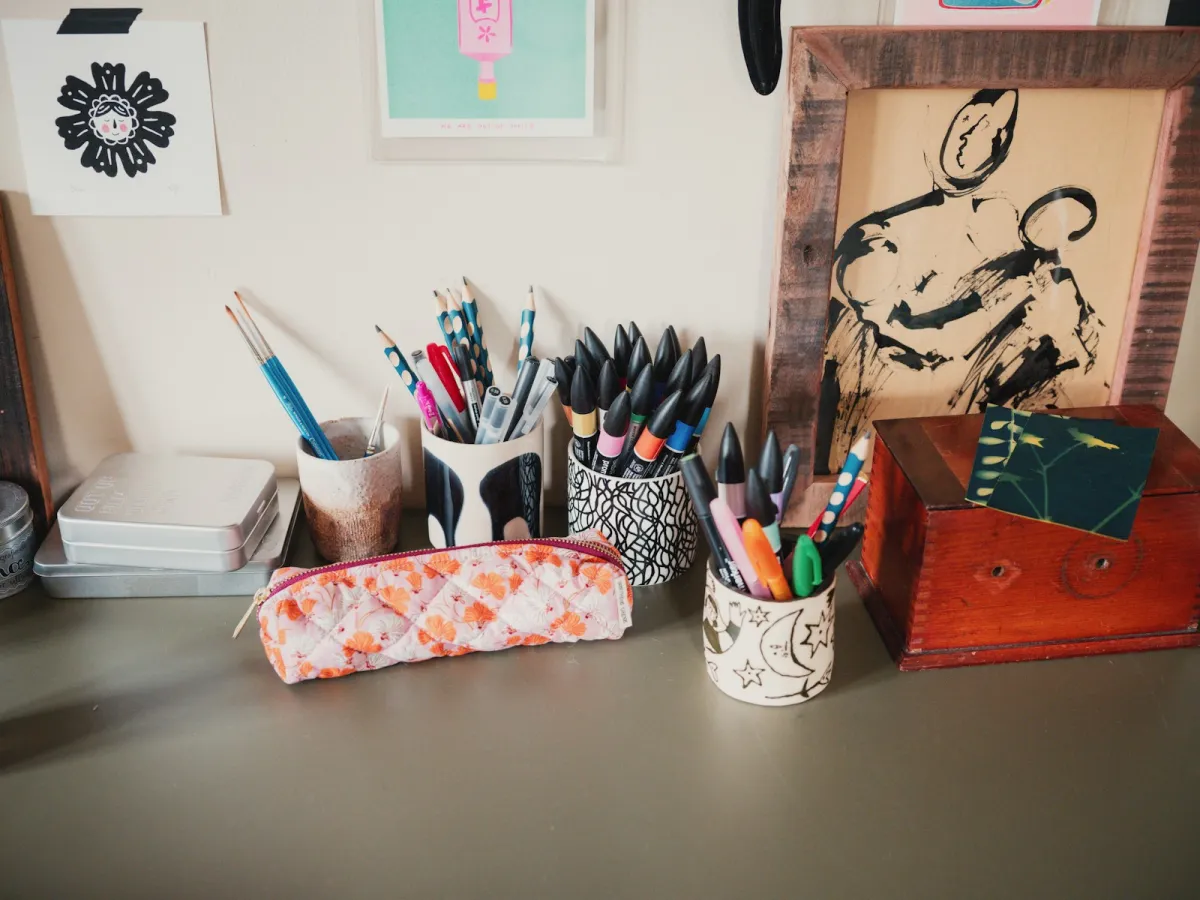 Colourful pens and pencils in ceramic pots with a floral pencil case on a desk