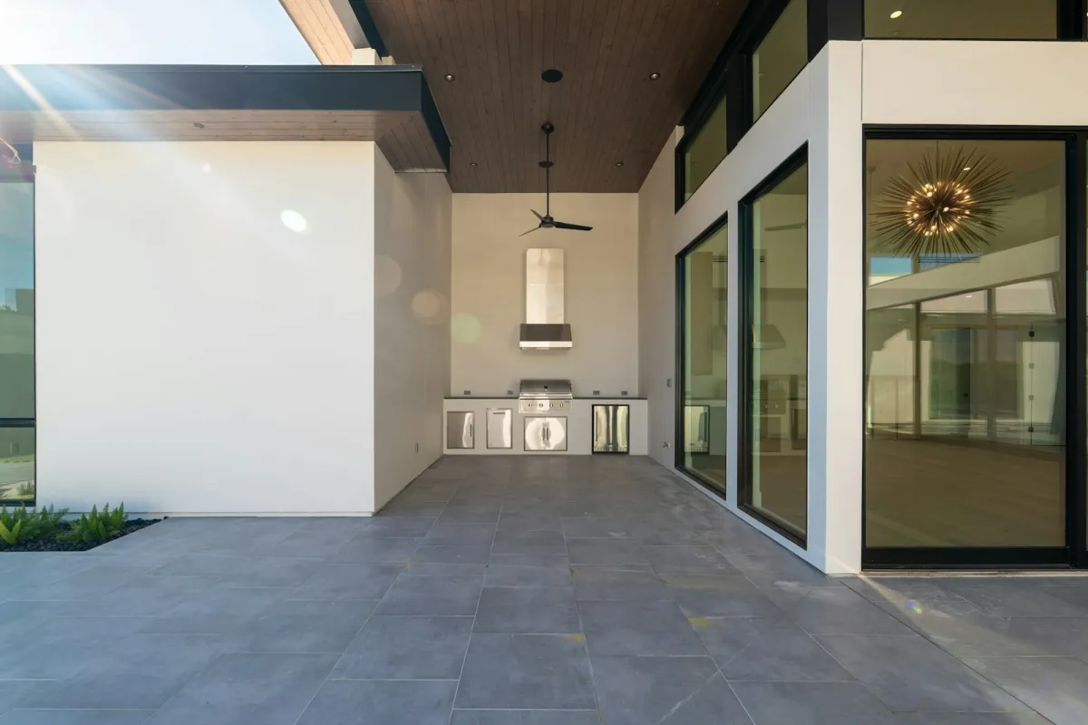 A covered modern patio with a built-in stainless steel grill, cabinets and a fridge