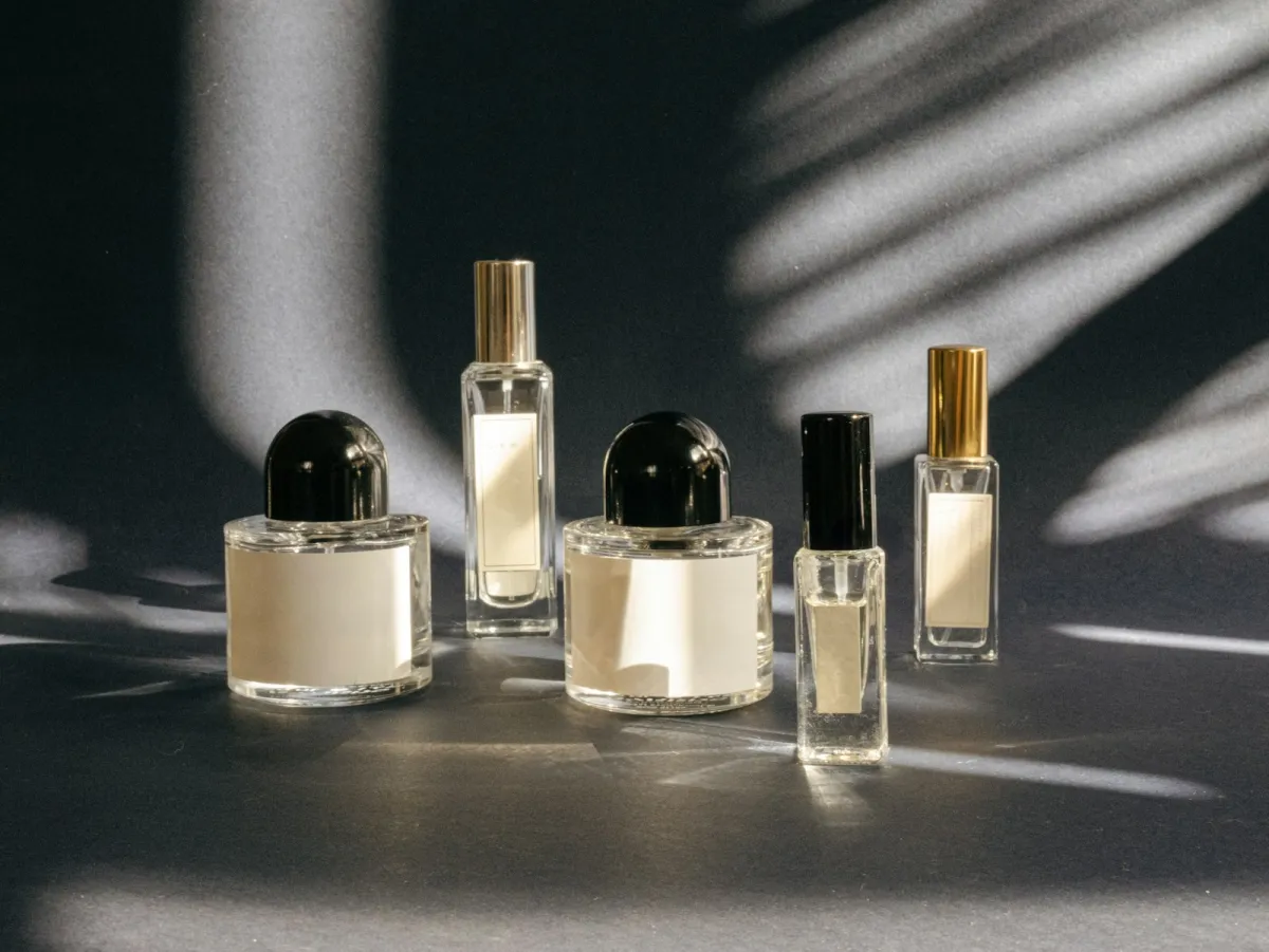 Several unbranded glass perfume bottles on a dark surface with leaf shadows