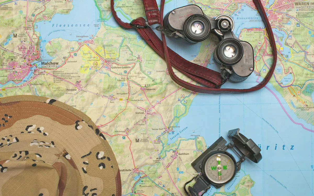 Binoculars, a compass and a sun hat lying on a paper map Binoculars, a compass and a sun hat lying on a paper map