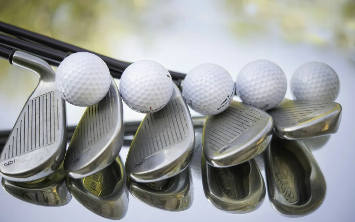 A row of golf irons with golf balls resting on the club heads A row of golf irons with golf balls resting on the club heads