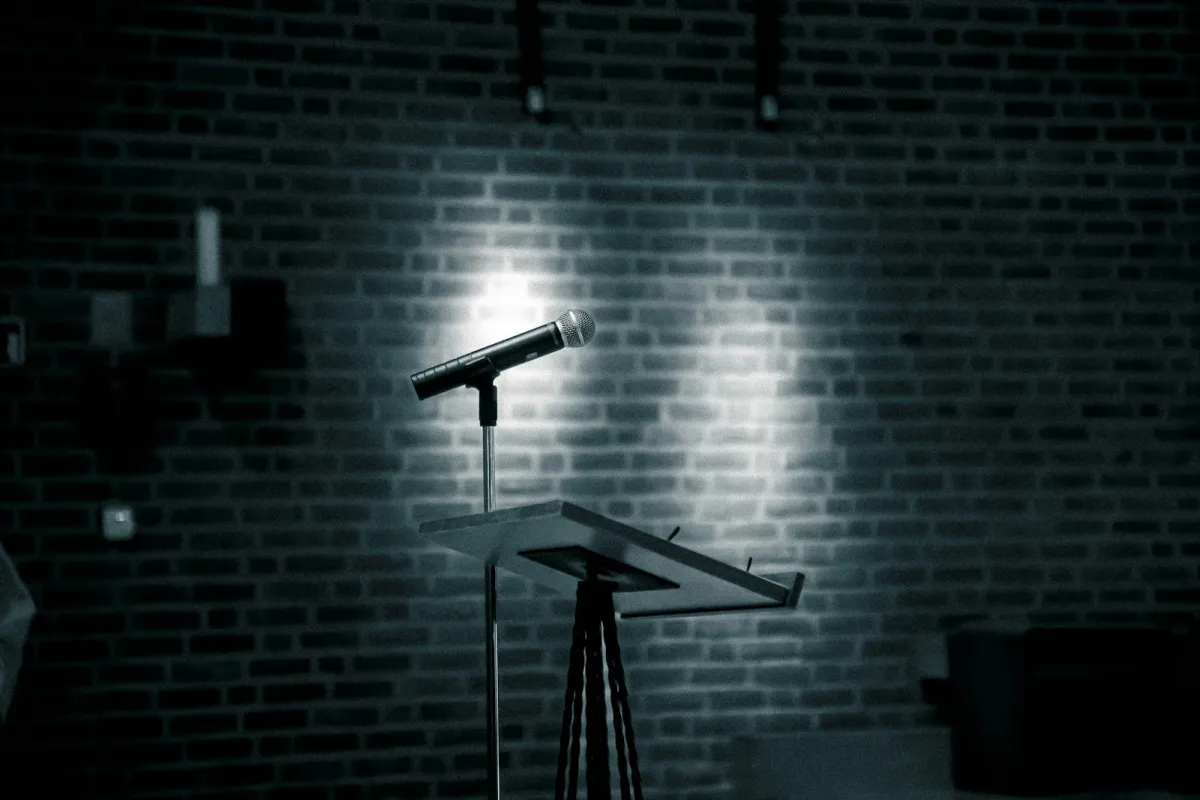 A microphone on a stand lit by a spotlight against a brick wall A microphone on a stand lit by a spotlight against a brick wall