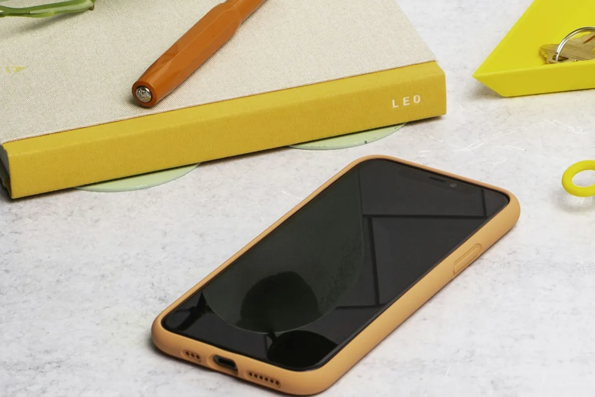 A smartphone in an orange case on a grey worktop beside a yellow notebook and pen A smartphone in an orange case on a grey worktop beside a yellow notebook and pen