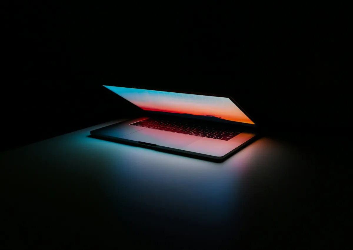 A half-open laptop glowing in a dark room A half-open laptop glowing in a dark room