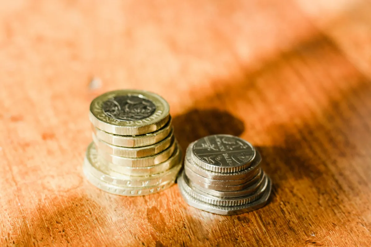 Two small stacks of British pound and 5p coins on a wooden table Two small stacks of British pound and 5p coins on a wooden table