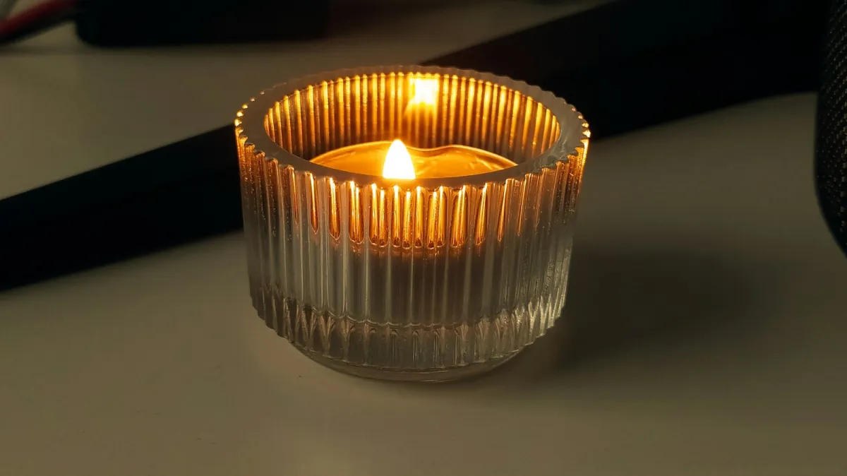 A lit tealight candle inside a ribbed glass holder on a pale table A lit tealight candle inside a ribbed glass holder on a pale table