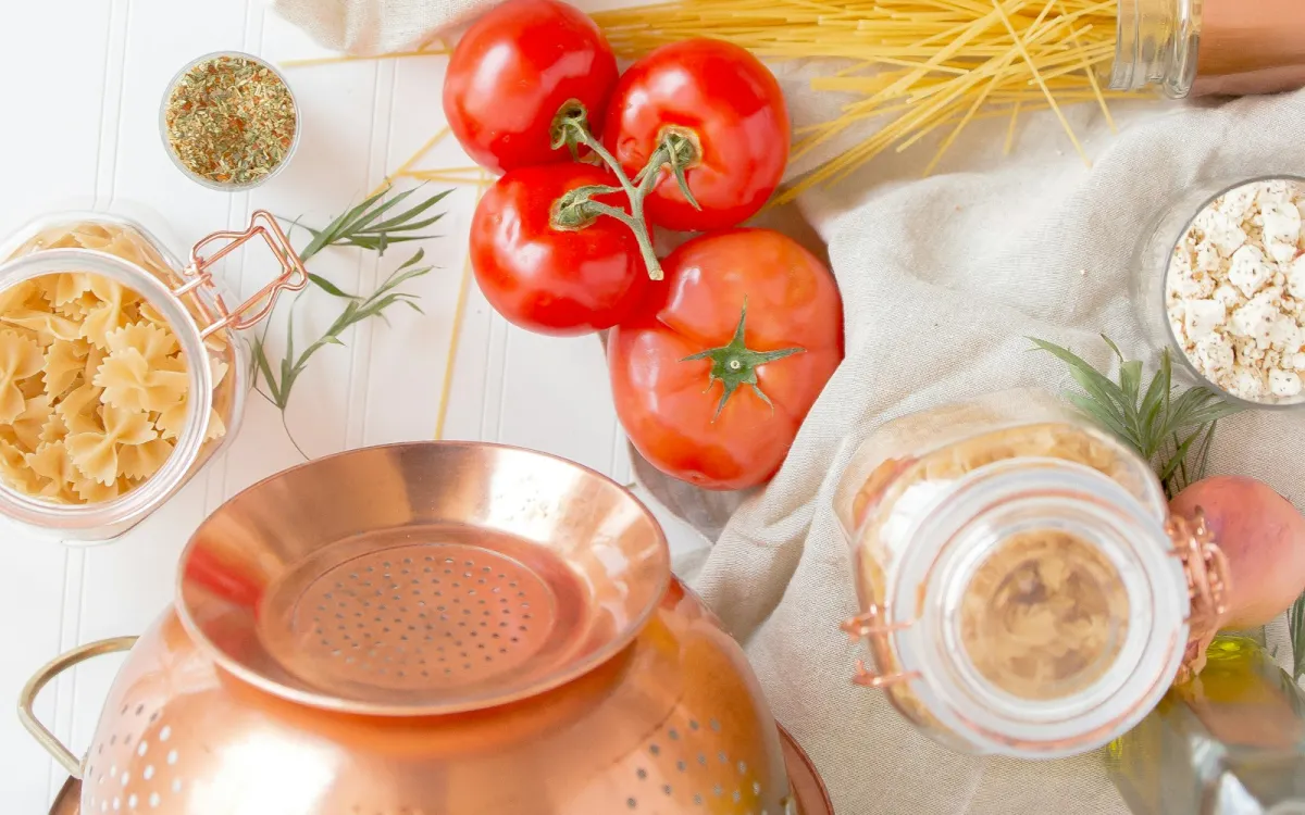 Fresh tomatoes, dried spaghetti, farfalle in a jar and a copper colander on a kitchen table Fresh tomatoes, dried spaghetti, farfalle in a jar and a copper colander on a kitchen table
