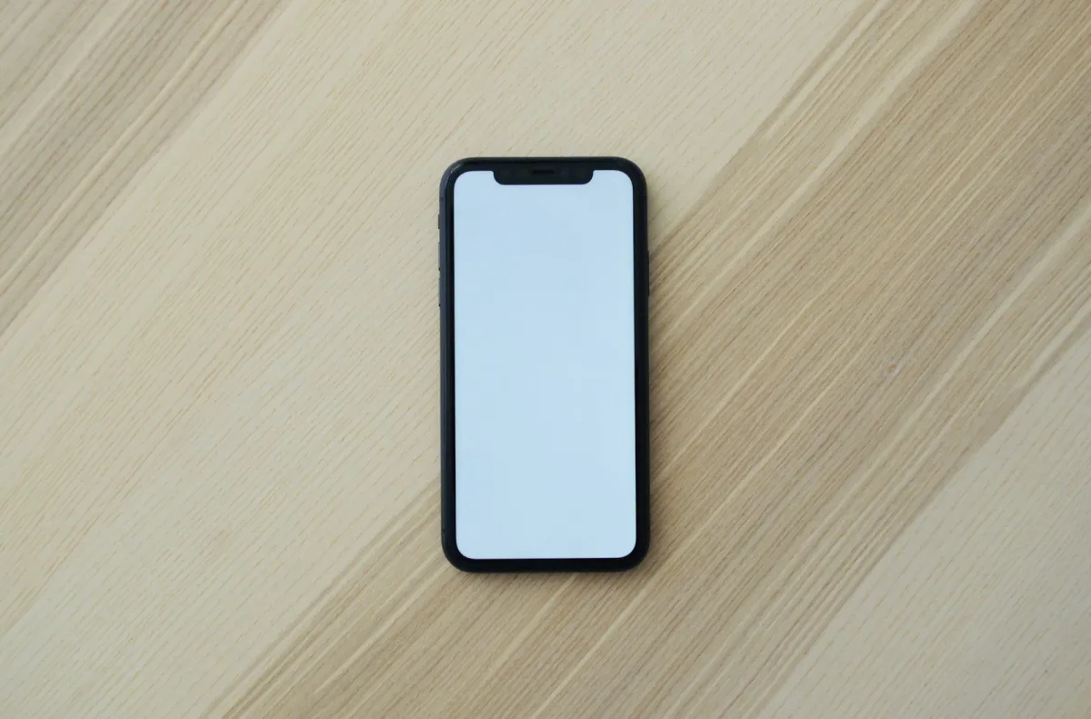 A black smartphone with a blank white screen lying on a light wooden table A black smartphone with a blank white screen lying on a light wooden table
