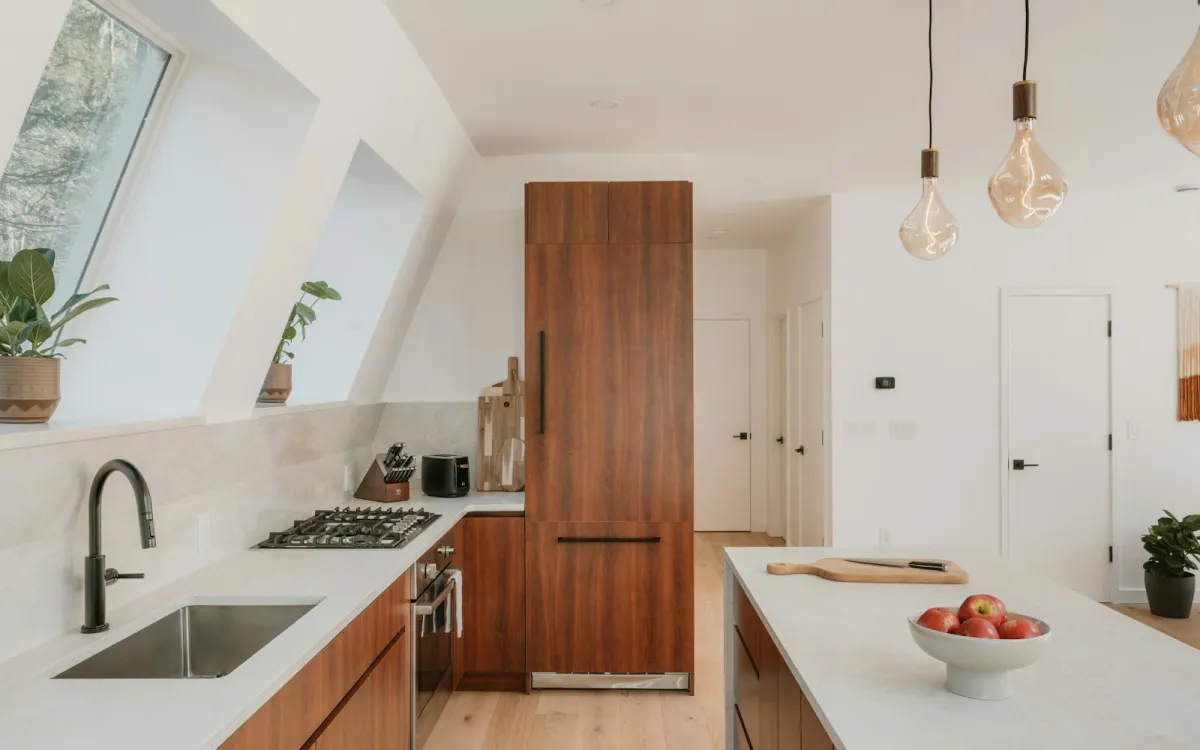 A bright modern kitchen with wood cabinets, a gas hob, built-in oven and a stone island