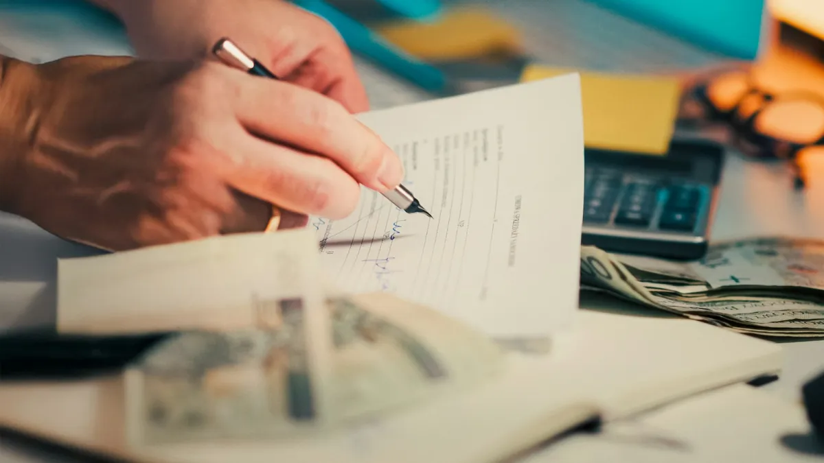 Hands signing a paper document on a desk next to a calculator