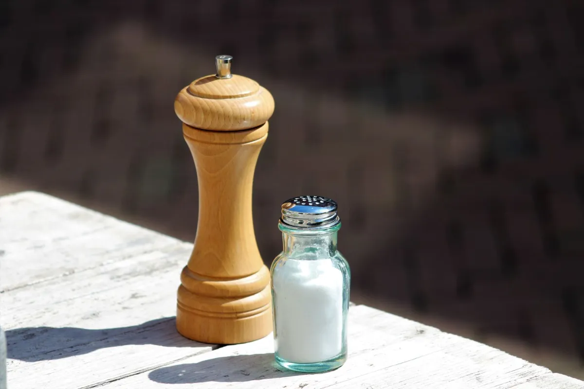 A wooden pepper mill and a glass salt shaker on a sunlit wooden table