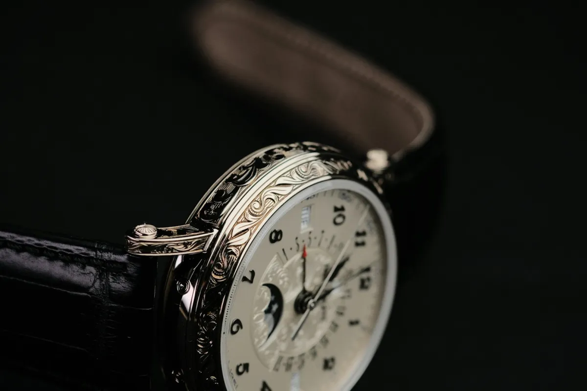 Close-up of an engraved steel watch case and dial on a leather strap against a dark background Close-up of an engraved steel watch case and dial on a leather strap against a dark background