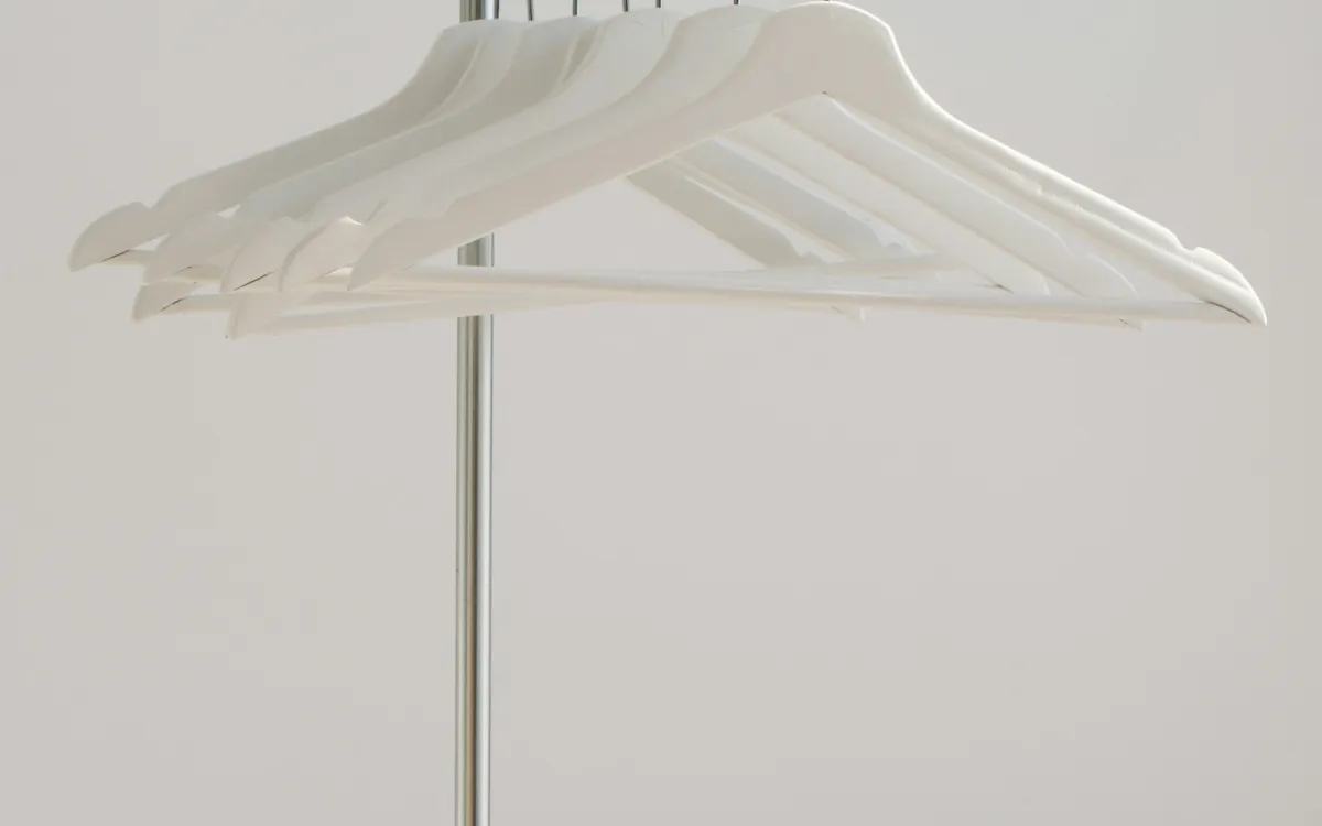 White wooden clothes hangers on a metal rail against a pale wall White wooden clothes hangers on a metal rail against a pale wall