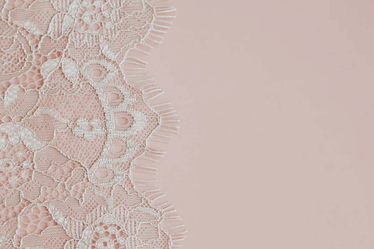 Delicate white lace fabric on a soft pink background