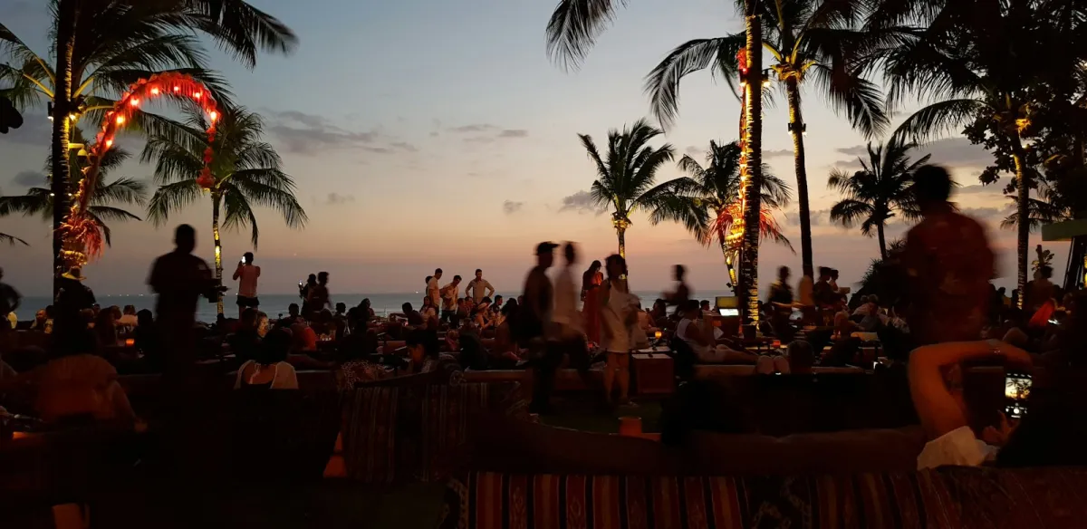 Palm trees and beach bar lights silhouetted against a Bali sunset over the sea