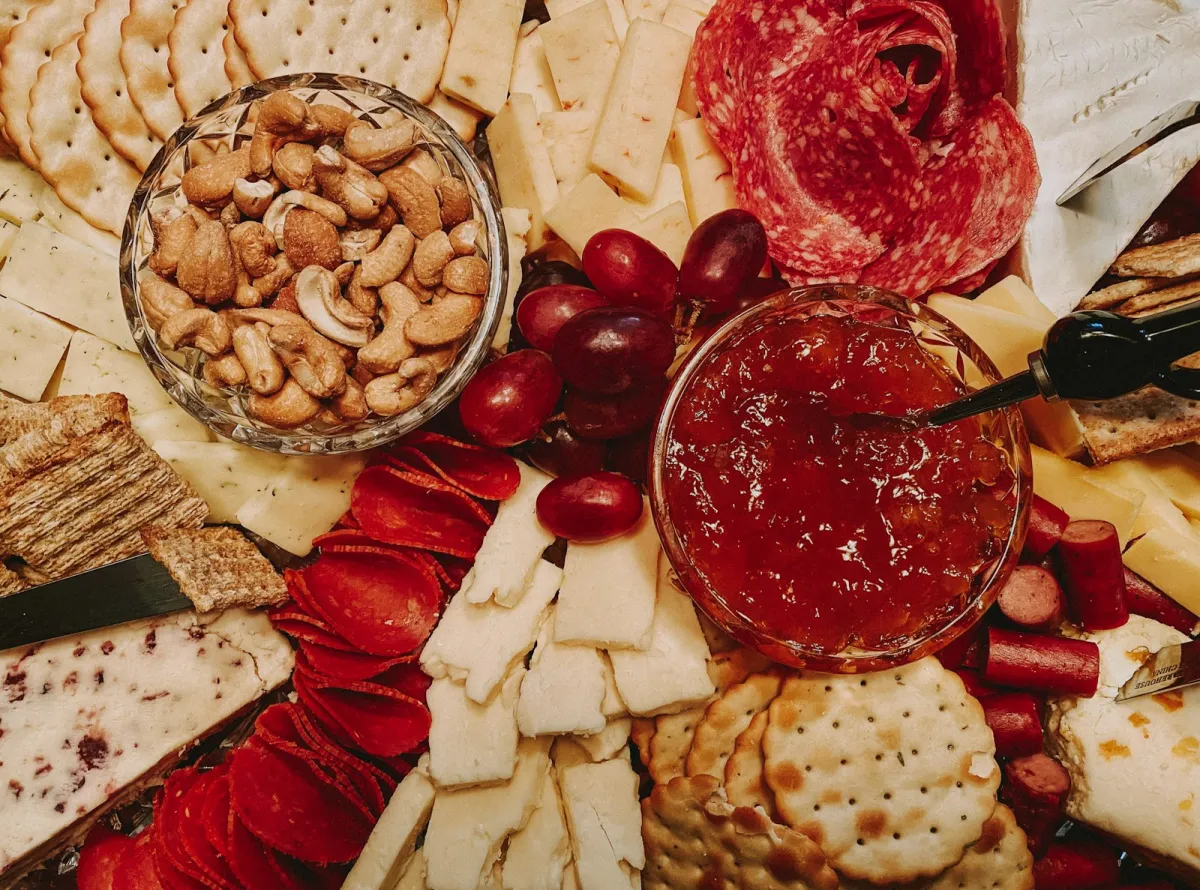 A platter of sliced cheeses, crackers, cured meats, grapes, nuts and chutney