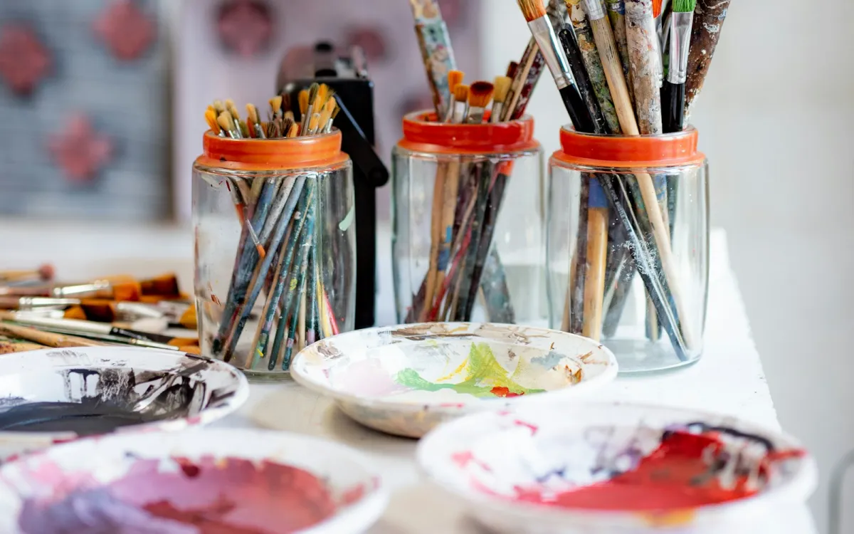 Jars of well-used paint brushes behind paint-smeared ceramic dishes on a studio table Jars of well-used paint brushes behind paint-smeared ceramic dishes on a studio table