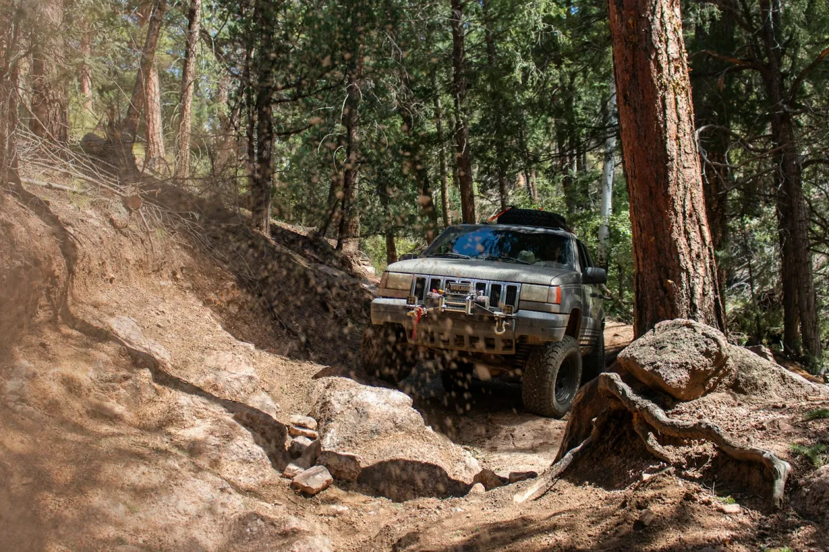 A grey off-road vehicle with a winch climbing a rocky forest trail A grey off-road vehicle with a winch climbing a rocky forest trail