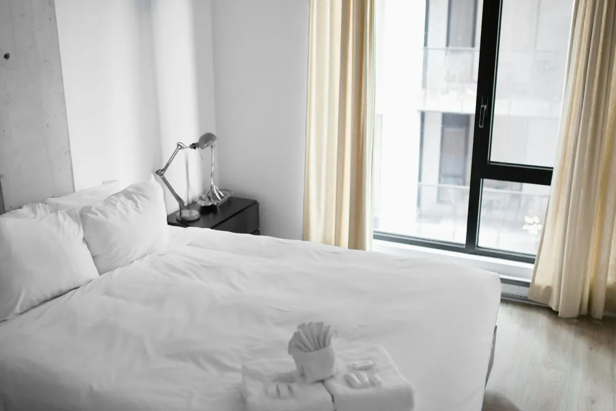 Made-up hotel bed with folded towels beside a large window Made-up hotel bed with folded towels beside a large window