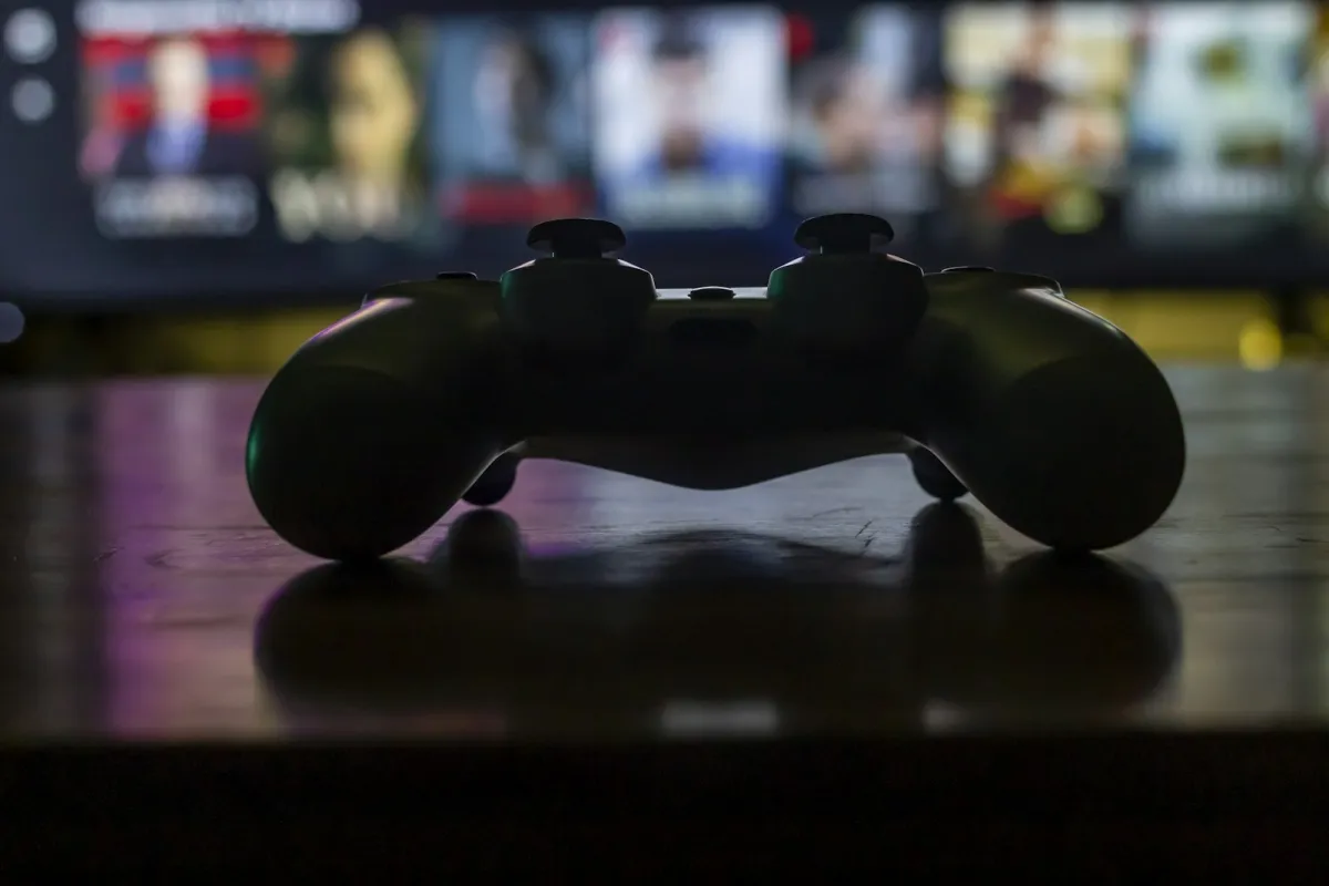 Silhouette of a games controller on a coffee table in front of a blurred TV screen Silhouette of a games controller on a coffee table in front of a blurred TV screen