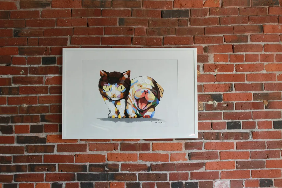 Framed colourful painting of a cat and a dog hanging on a brick wall