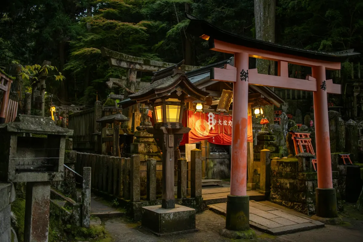 A red torii gate and glowing lanterns at a shrine in Kyoto at dusk