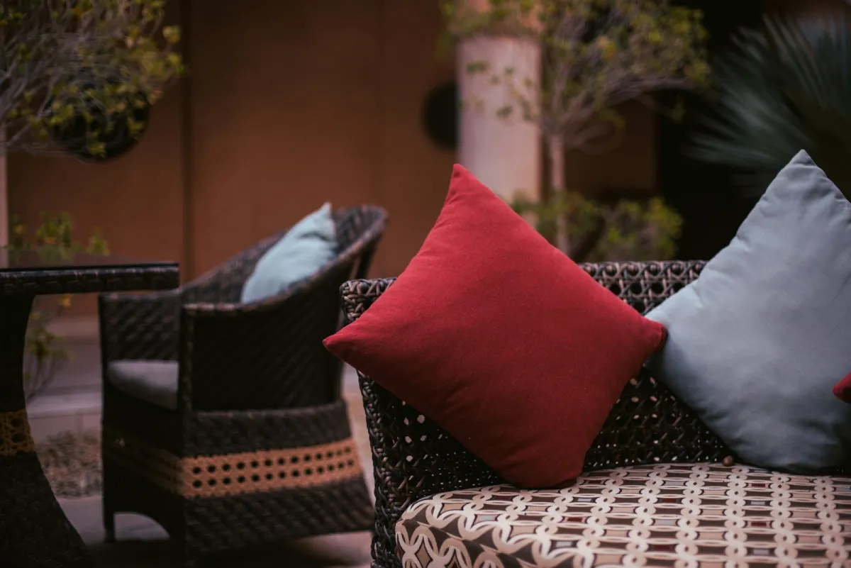 Dark woven rattan sofa and armchair with red and blue cushions on a garden patio Dark woven rattan sofa and armchair with red and blue cushions on a garden patio